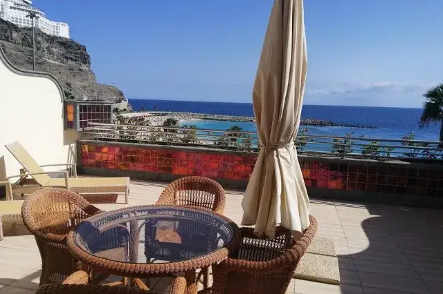 A panoramic view of the crystal-clear waters and golden sands of Amadores Beach, showcasing the elegant Holiday Club Playa Amadores resort, surrounded by palm trees and inviting sunshine.